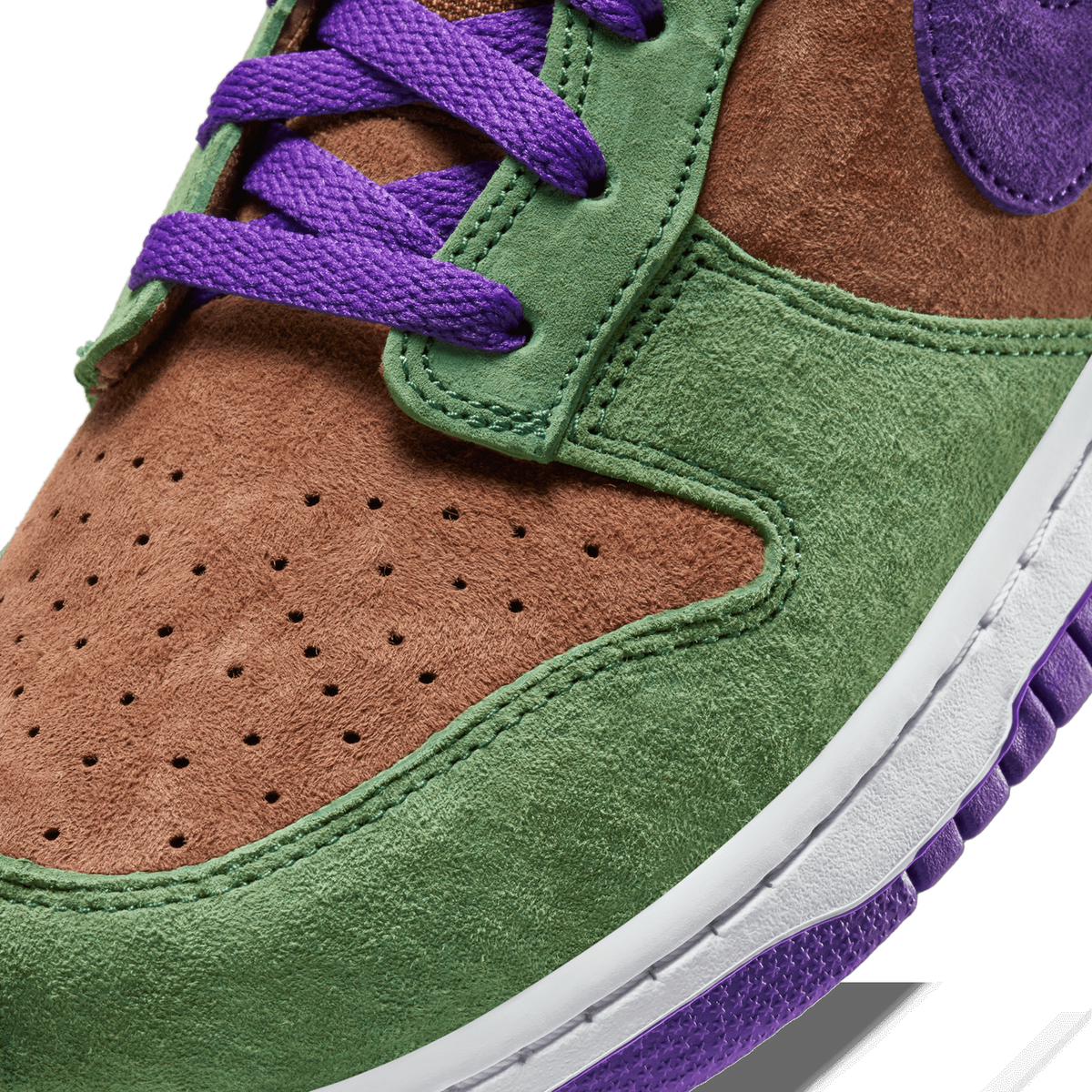 Close-up of a Nike Dunk Low toe box showing green and brown suede panels, perforated vamp, purple laces, and purple midsole with white trim.