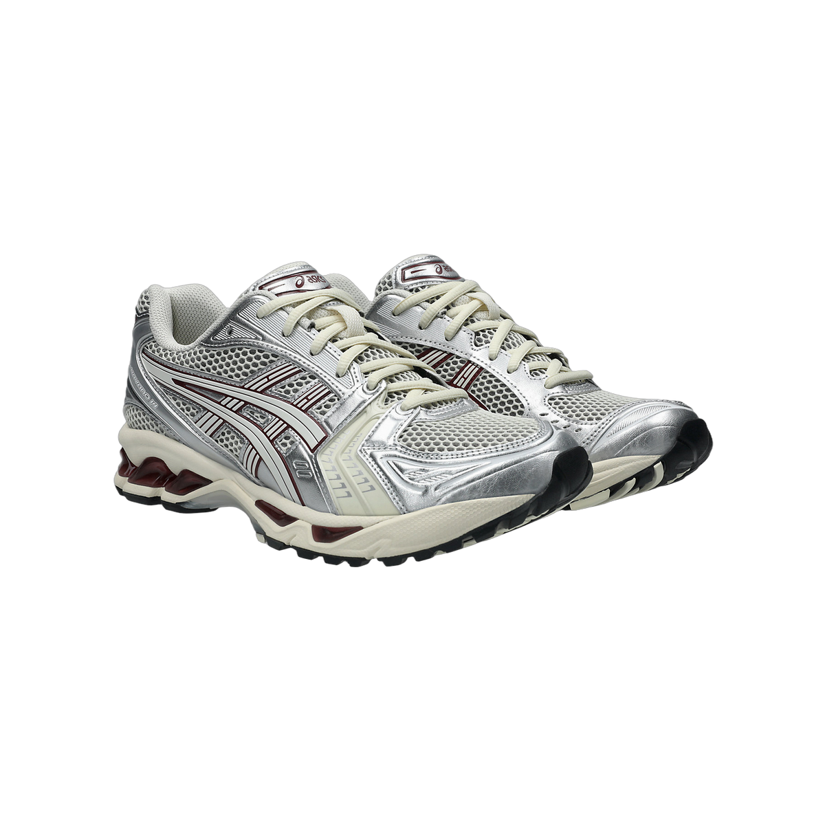 Pair of Asics Gel-Kayano 14 sneakers in silver and cream with maroon accents on the midsole, viewed from a front side angle.