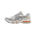 Side profile of a white, silver, and orange ASICS Gel-Kayano 14 running shoe with the toe pointing left, showing silver overlays, white mesh panels, and orange gel cushioning visible at the midsole and heel.
