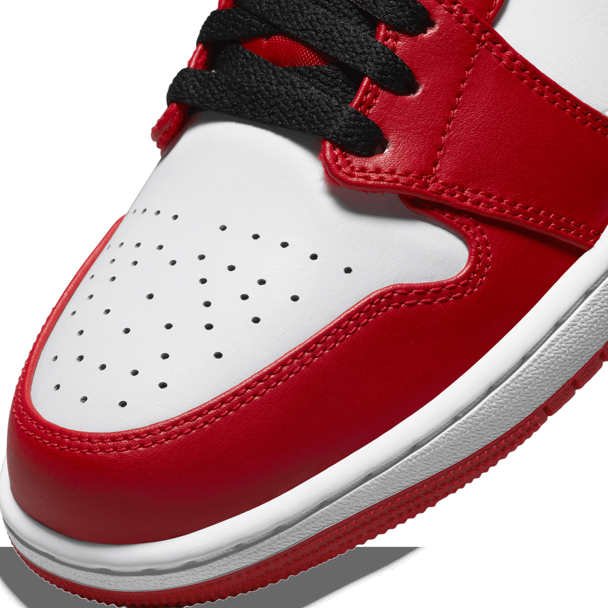 Close-up of the toe box and lacing area of a red, white, and black Air Jordan 1 Low, showing perforated white toe leather, red overlays, black laces, and the white midsole edge with red rubber outsole.