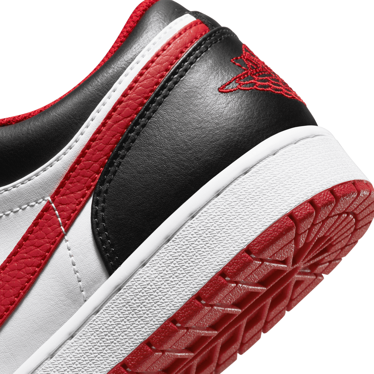 Close-up of the heel and outer side of a white, red, and black Air Jordan 1 Low, showing the black heel with red Jumpman embroidery, the red and white side panel, and the white and red rubber outsole tread.