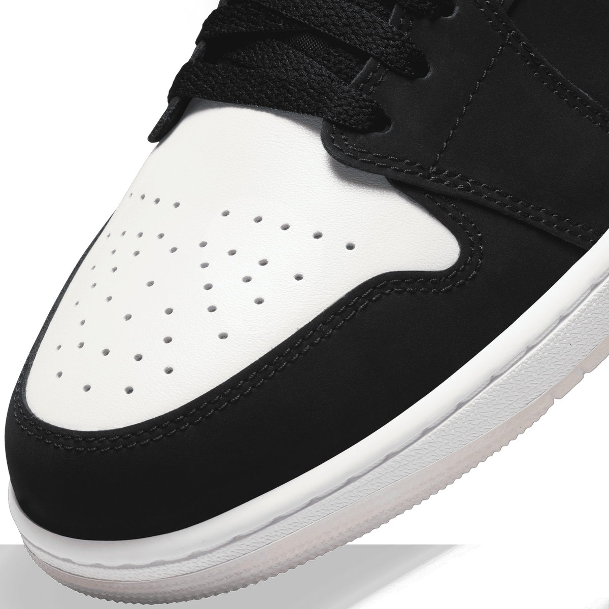Close-up of a black and white Air Jordan 1 Low toe box showing perforated leather, stitching, and black laces.