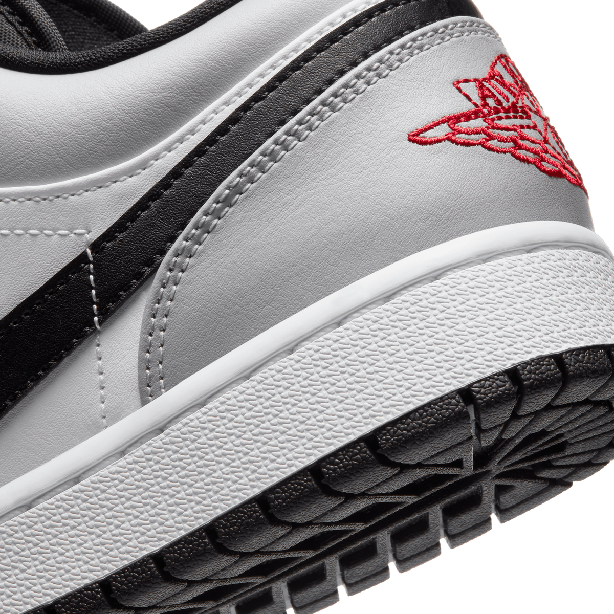 Close-up of a grey Jordan 1 Low heel showing the black swoosh, red embroidered Wings logo, and textured sole edge.