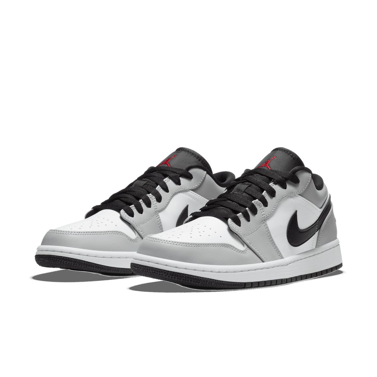 Pair of Air Jordan 1 Low sneakers in light smoke grey, white, and black with black Swoosh logos and red Jumpman embroidery on the tongue, angled toward the left