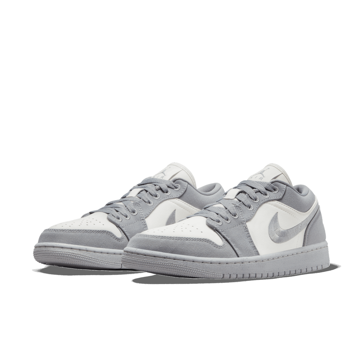 A pair of grey and white low-top Air Jordan 1 sneakers angled side by side toward the left, showing the grey canvas panels, white leather toe boxes and mudguards, and embroidered grey Swoosh logos on the sides.