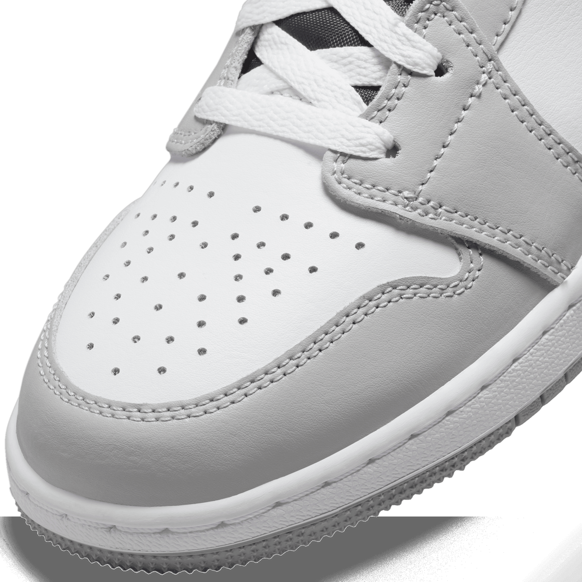 Close-up of the toe box of a grey and white Jordan 1 Mid sneaker showing perforated holes, white laces, and stitched overlays.