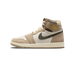 Side profile of a single high-top sneaker with the toe pointing left, showing beige and tan nubuck panels, a cream leather mid-section, an olive-green canvas Swoosh, and a gold Air Jordan wings logo on the ankle collar.