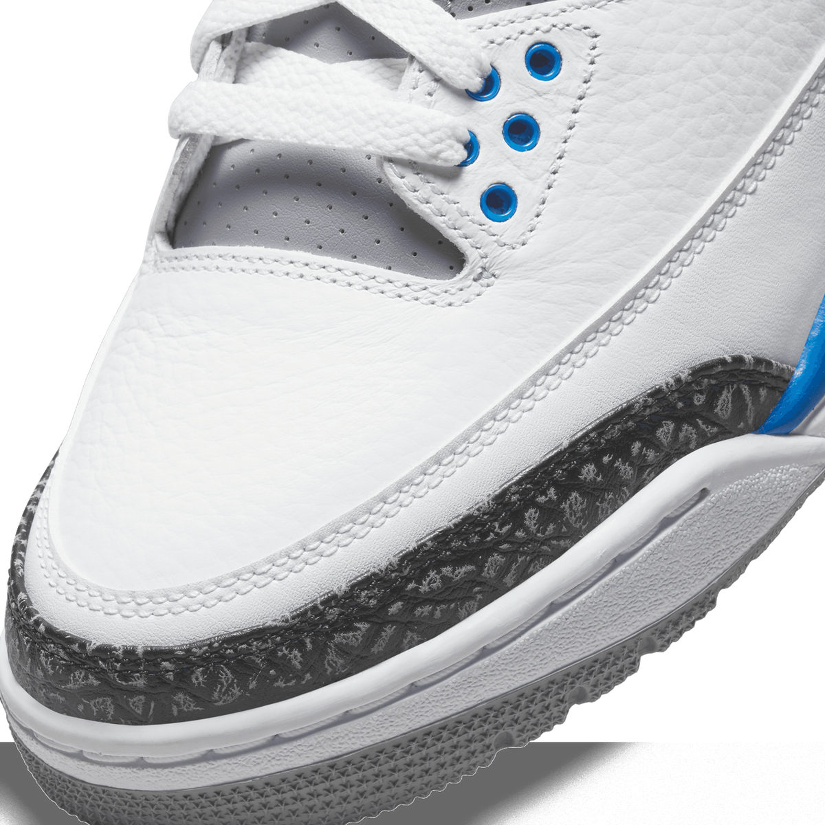 Close-up of the toe box of a white Jordan 3 Retro with grey elephant print trim, blue eyelets, and white laces.