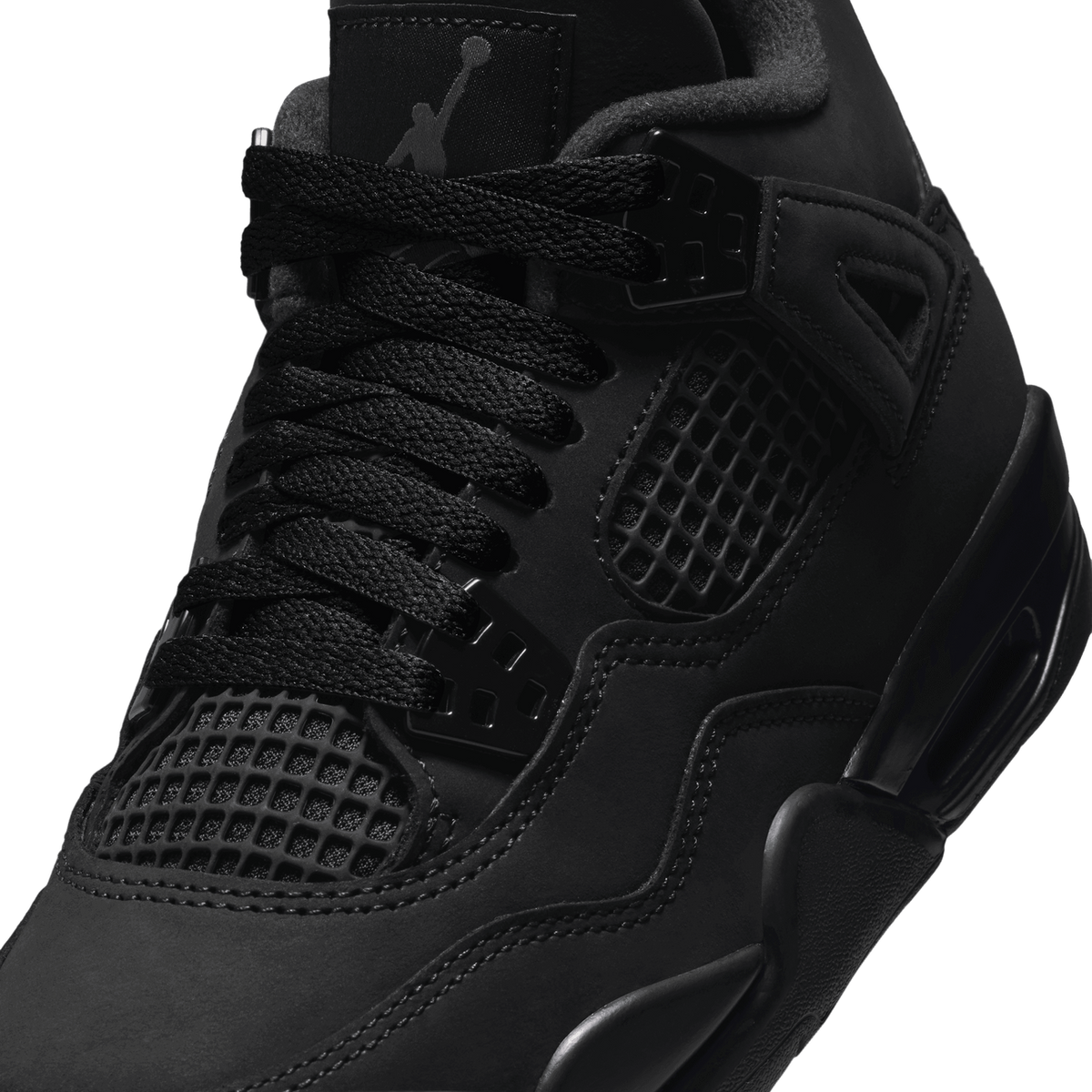 Close-up view of an all-black Air Jordan 4 sneaker showing the mesh side panel, lacing system, plastic eyelet wing, and Jumpman tongue tag.