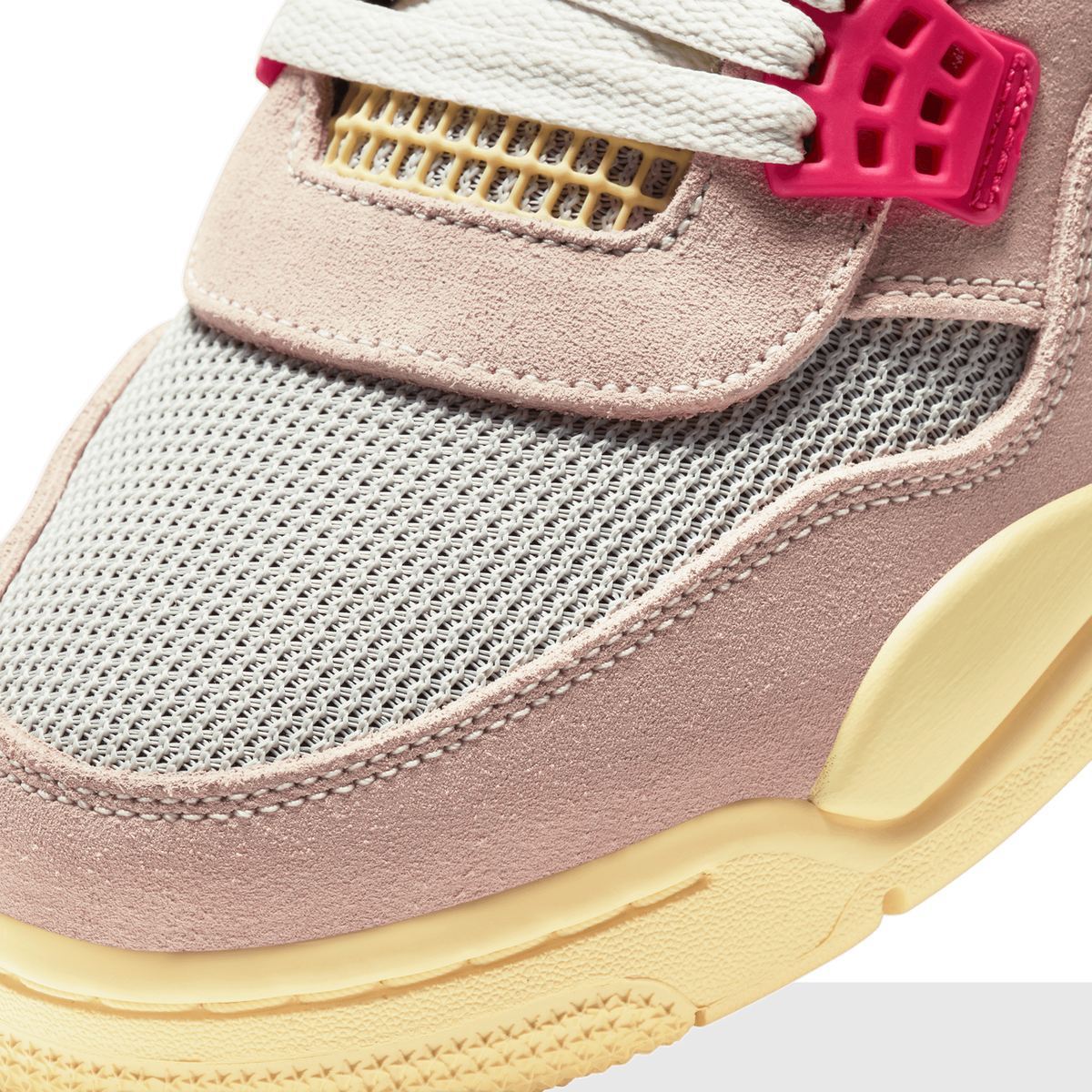 Close-up detail of a sneaker's toe box and lacing area showing pinkish-tan suede overlays, grey mesh panels, cream laces, a yellow mesh eyelet, a hot pink lace lock, and a pale yellow midsole edge.