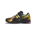Side view of a black New Balance 1906U sneaker with a yellow N logo, gradient yellow-green-orange detailing, pink accents on the midsole, and Bricks & Wood branding on the side panel