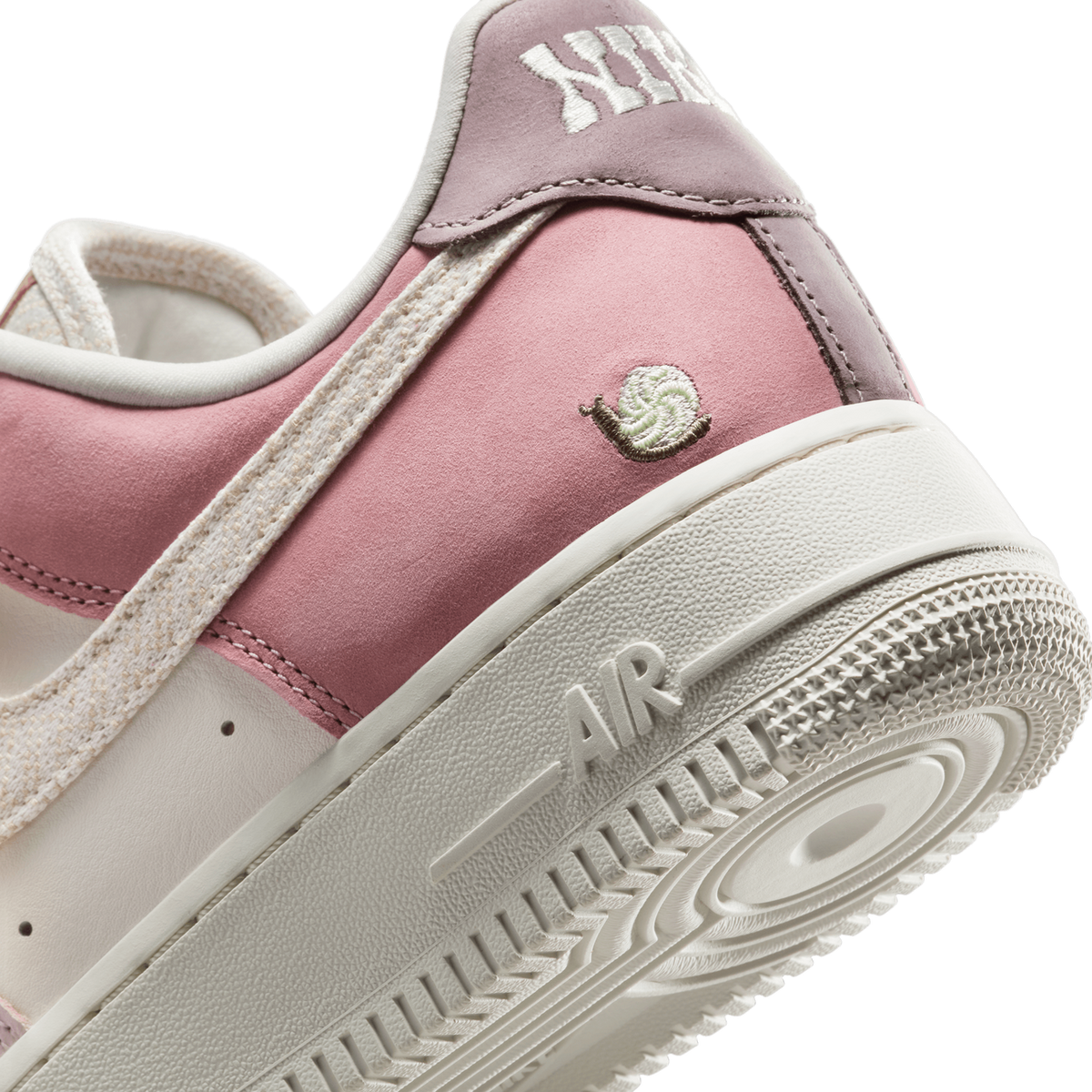 Close-up angled view of a pink and mauve Nike Air Force 1 Low heel showing a small embroidered snail patch and the Air logo on the sole