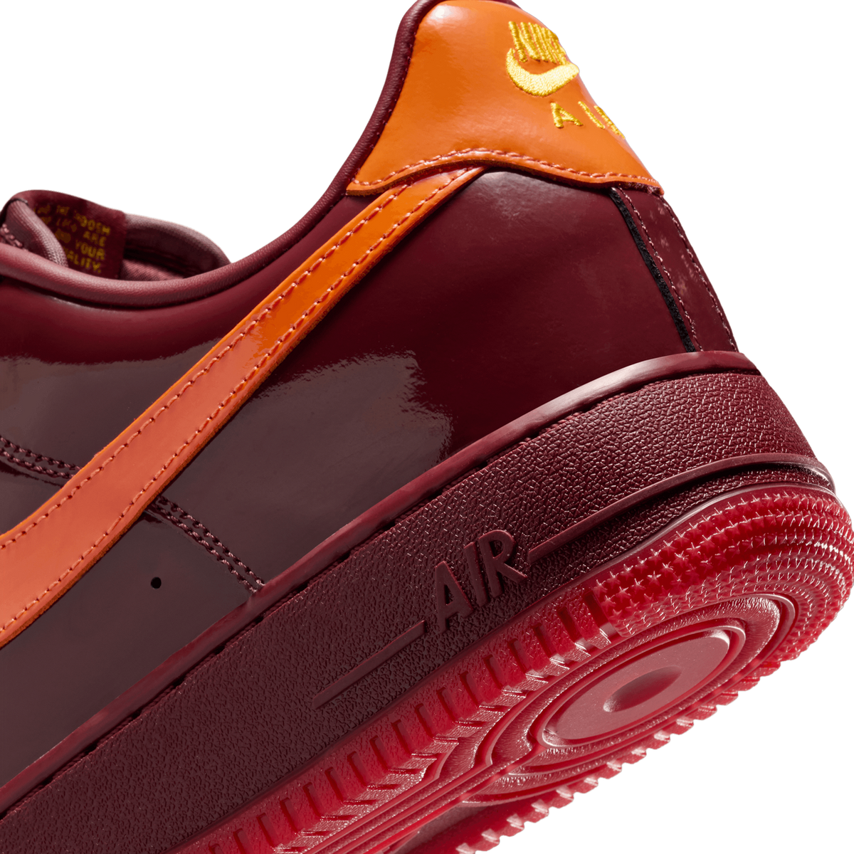 Close-up angled view of a dark red patent leather Nike Air Force 1 showing the orange heel tab with gold Swoosh logo and textured midsole with AIR text