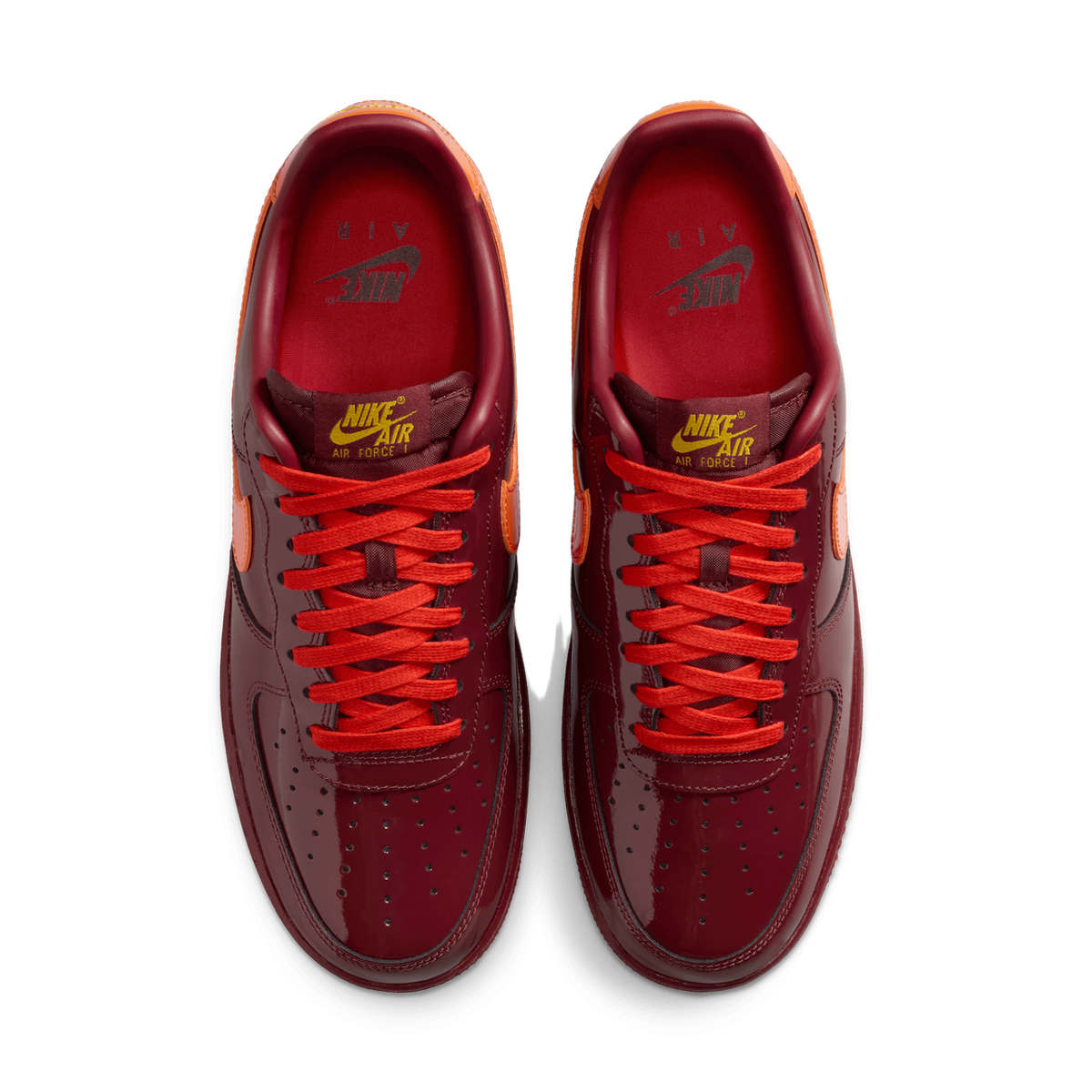 Top-down view of a pair of dark red patent leather Nike Air Force 1 Low sneakers with orange Swoosh logos and red laces, facing toward each other.