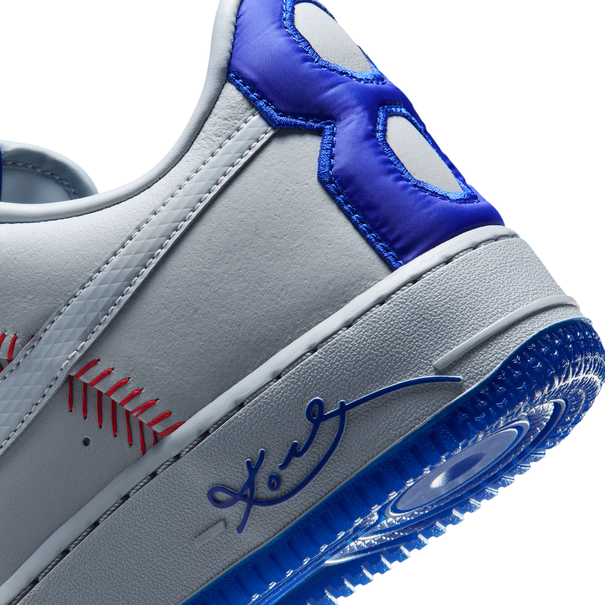 Close-up of the heel area showing grey leather with red baseball-stitch embroidery, a blue signature logo, and a blue pull tab with cutout details near the midsole.