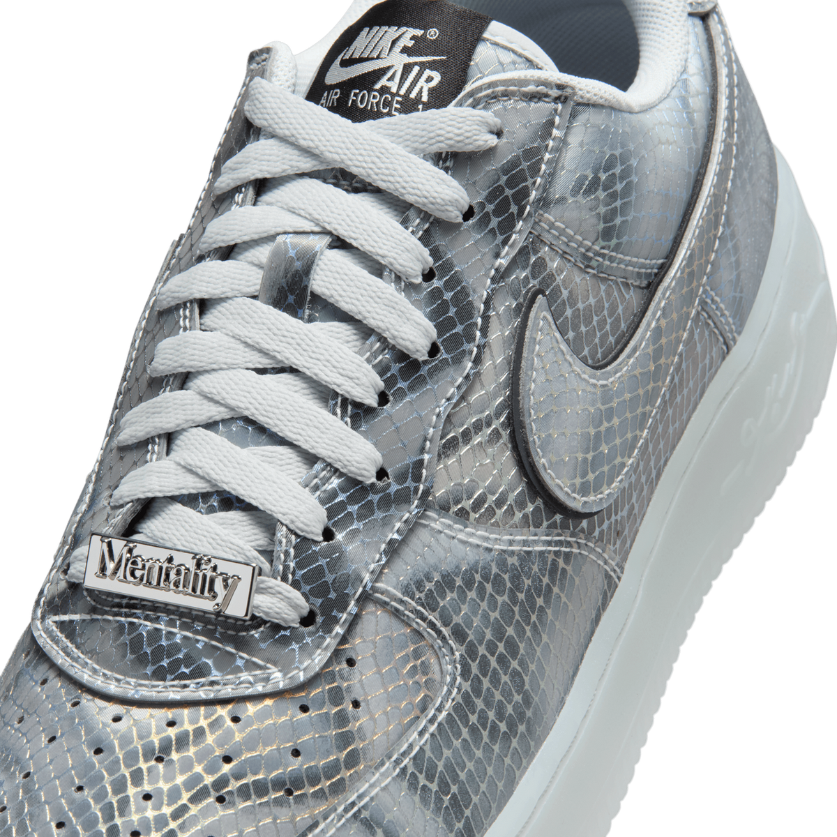 Close-up of a silver metallic snakeskin-patterned sneaker with white laces, a black Nike Air Force 1 tongue tag, a silver 'Mentality' metal plate on the lacing, and a Nike swoosh on the side, showing the toe and collar area.