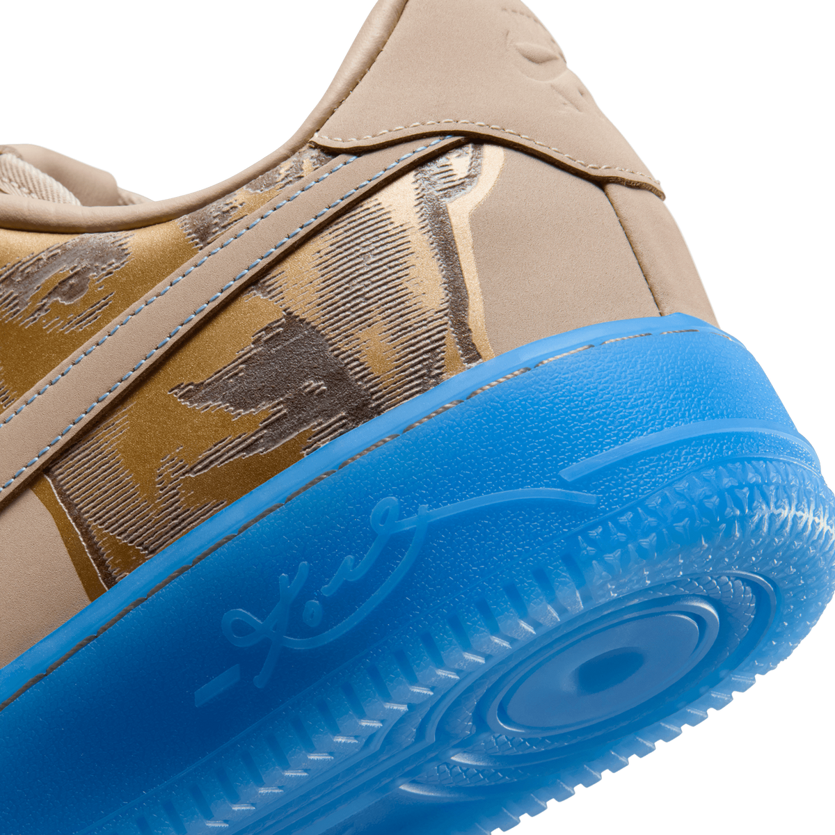 Close-up of the heel and lateral side of a beige Nike Air Force 1 Low, showing the textured tan nubuck upper with gold-and-brown printed artwork, a blue translucent midsole and outsole edge with embossed script branding, and blue stitching along the