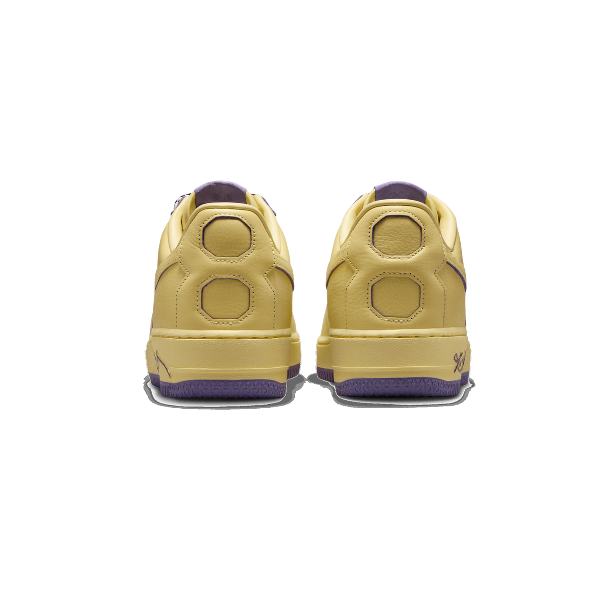 Rear view of a pair of pale yellow Nike Air Force 1 Low sneakers with purple accents on the heel tabs, swooshes, and outsole edges, showing the octagonal heel panels and a script signature on the heel.