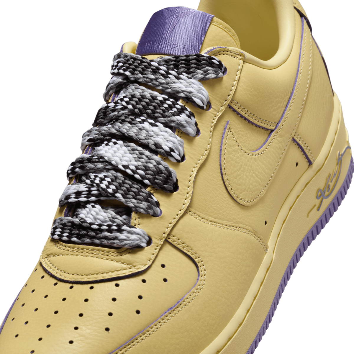 Close-up of a yellow Nike Air Force 1 Low with purple accents, showing the laces with black-and-white checkered pattern, the perforated toe box, the Nike swoosh on the side panel, and the purple tongue tag reading 'Air Force 1'.