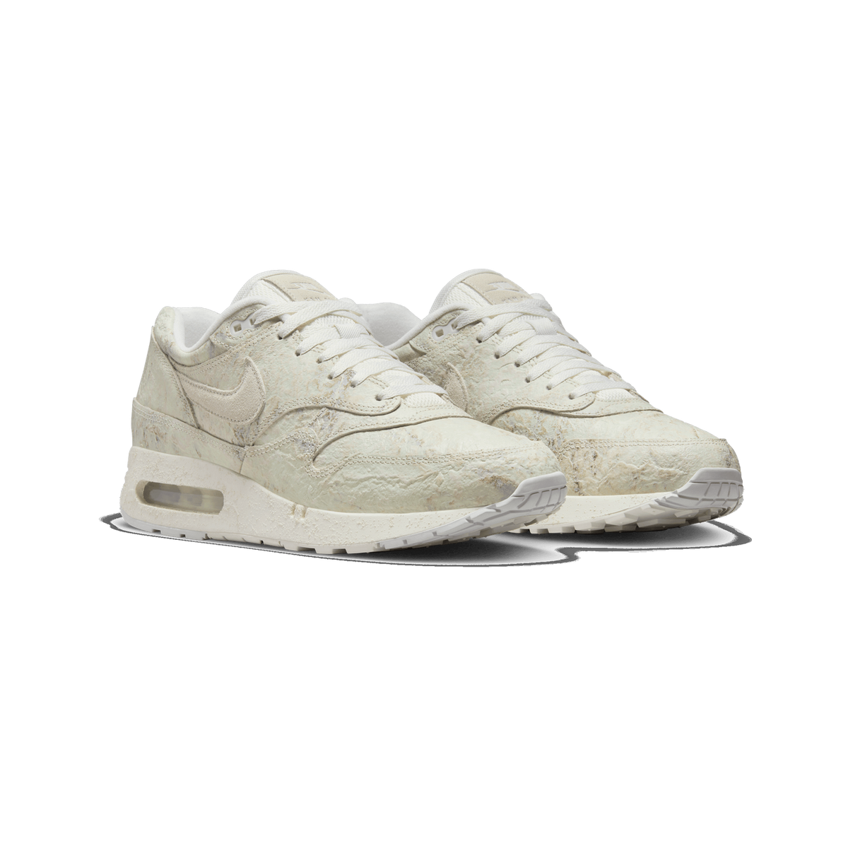 Pair of cream-white Nike Air Max 1 sneakers with a textured, mottled upper, angled toward the left, showing the lacing, Swoosh logos, and the visible Air unit in the midsole.