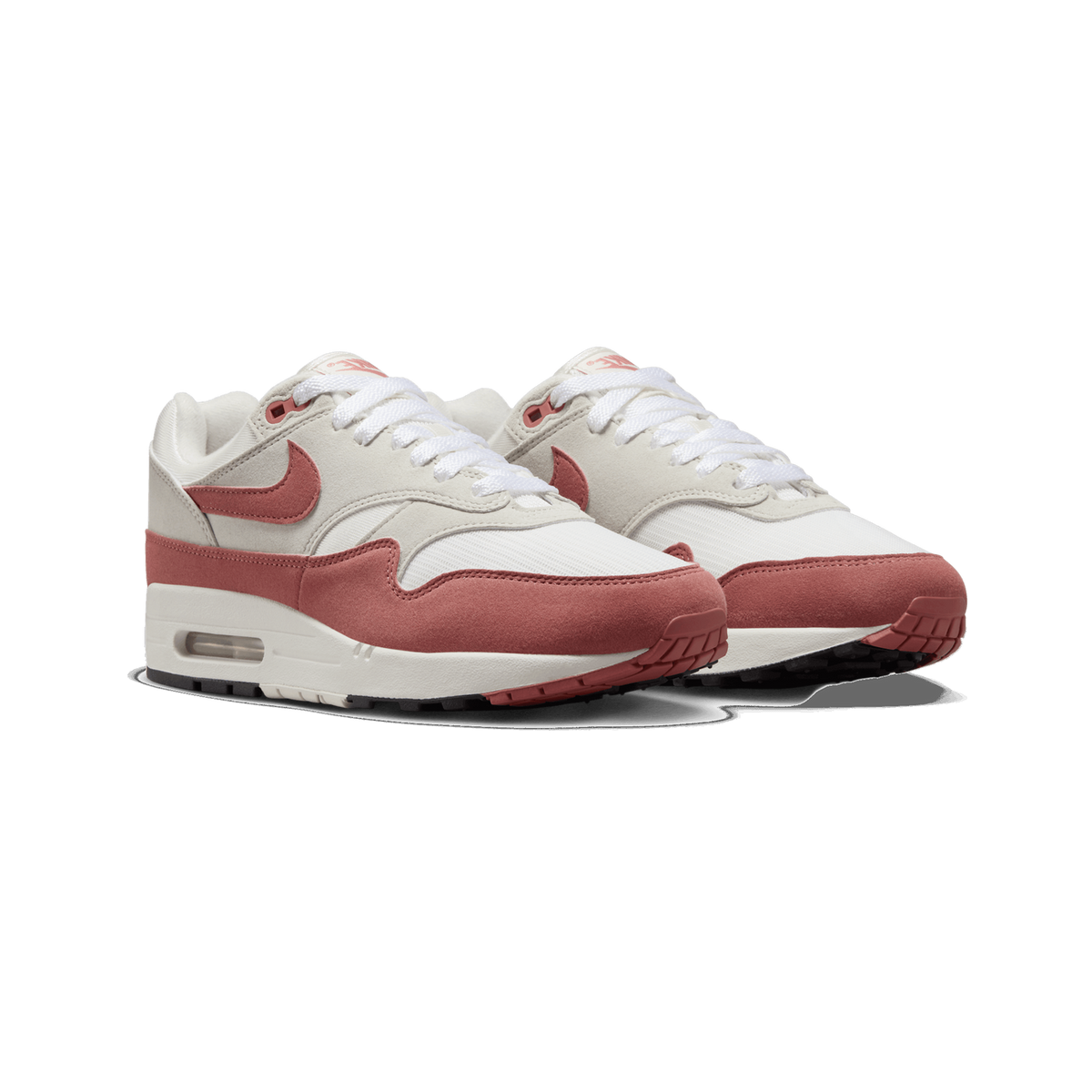 A pair of Nike Air Max 1 sneakers shown side by side at a three-quarter angle, with a red-pink suede toe and heel overlay, a red Swoosh on each shoe, white laces, and a cream-white midsole with a visible Air unit window.