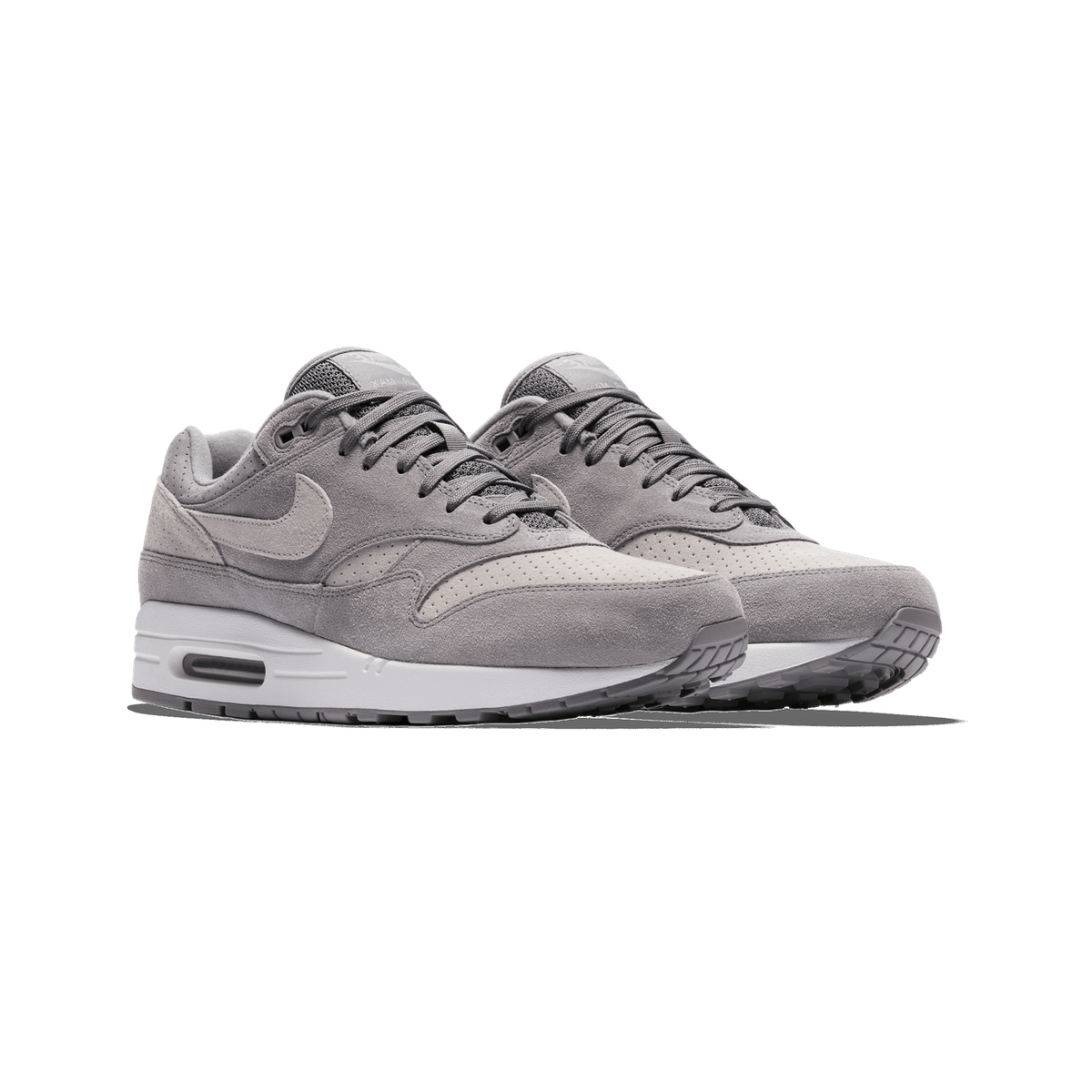 A pair of grey suede Nike Air Max 1 sneakers with white midsoles, shown side by side at a three-quarter angle with the toes pointing toward the viewer and slightly left, with grey laces and perforated toe panels.