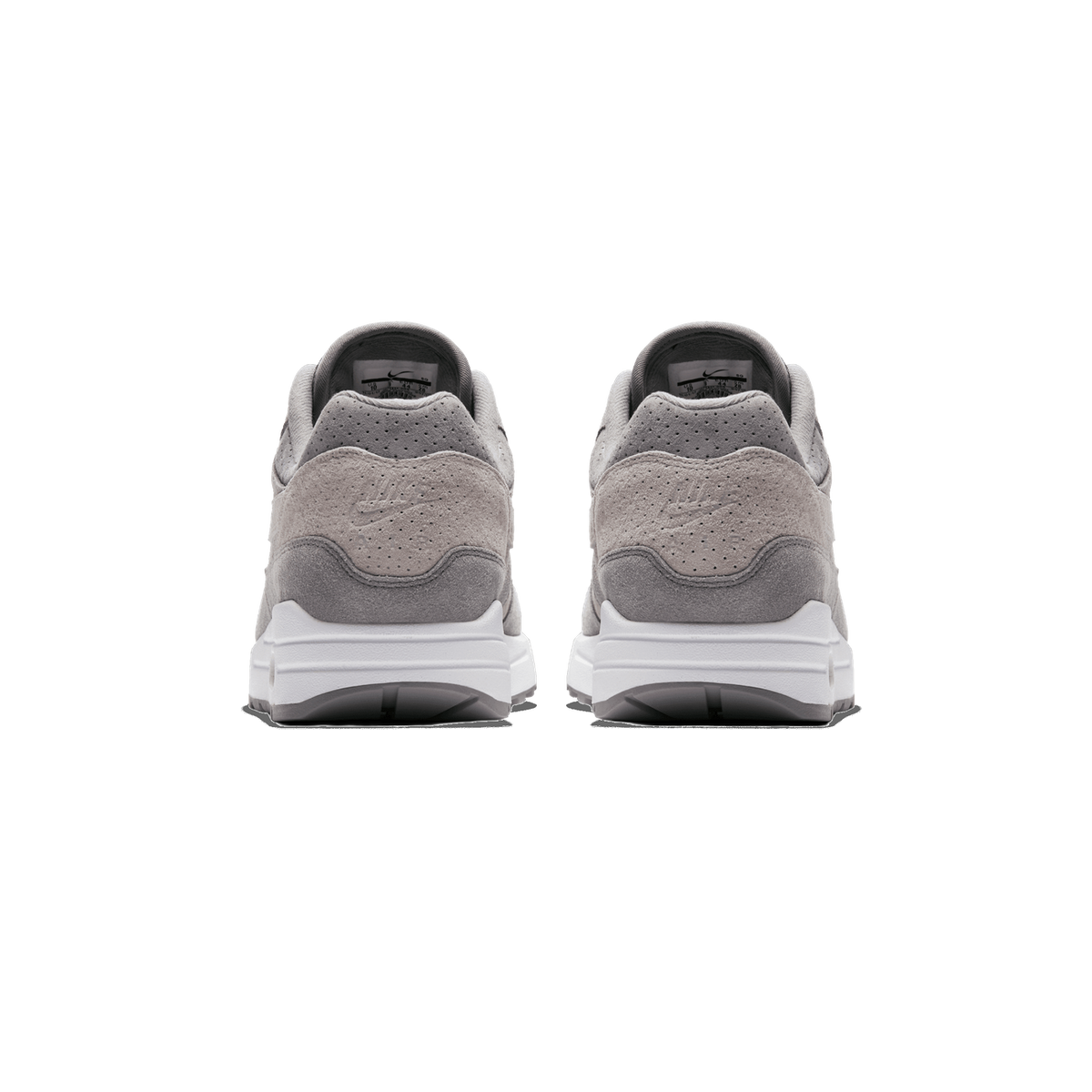Rear view of a pair of grey suede Nike Air Max 1 sneakers standing side by side, showing the perforated heel tabs with embossed Nike swooshes, pull tabs, and white midsoles with grey outsole edges.