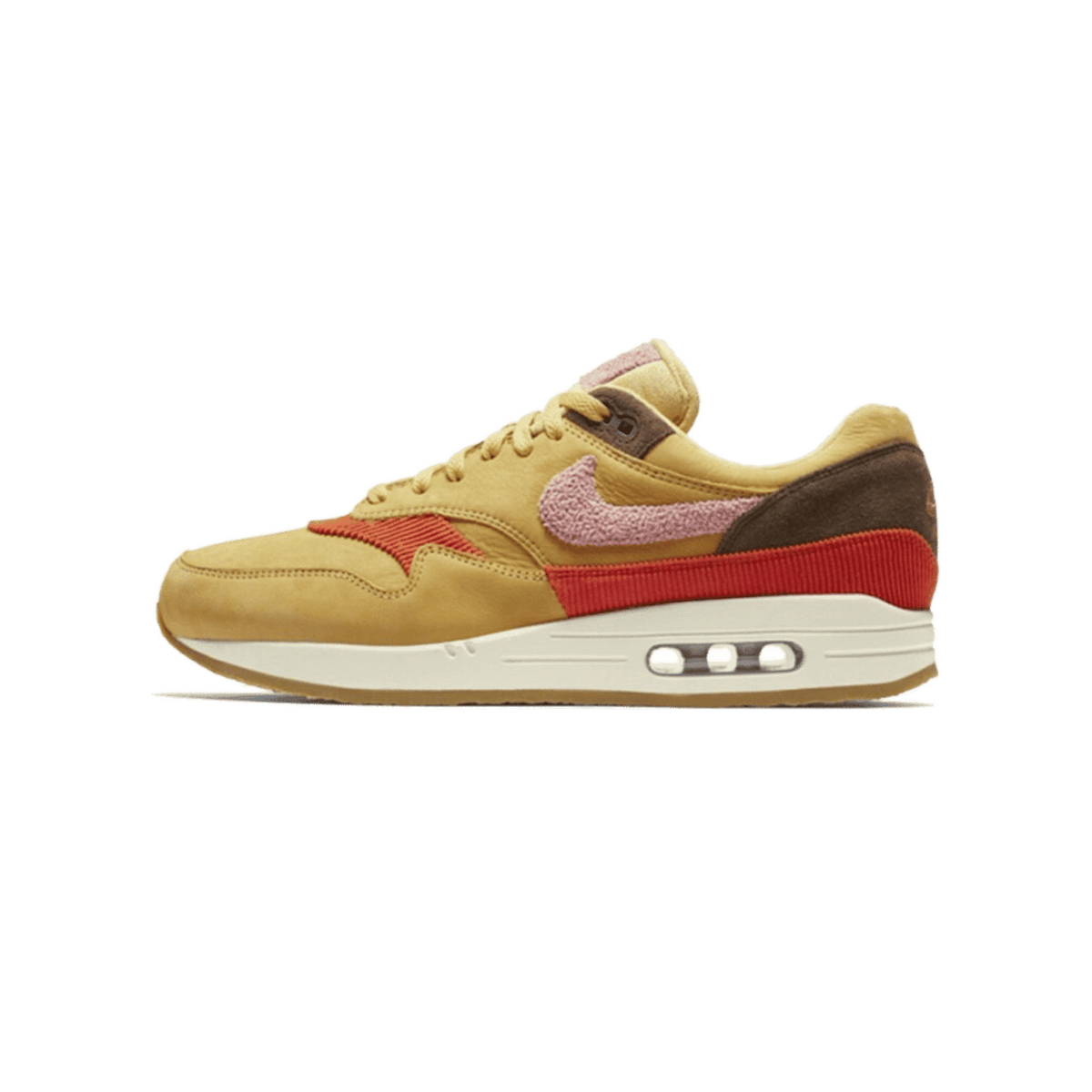 Left Nike Air Max 1 sneaker in wheat gold with rust red corduroy panel, pink fuzzy swoosh, and brown suede heel, shown from the outside with toe pointing left.