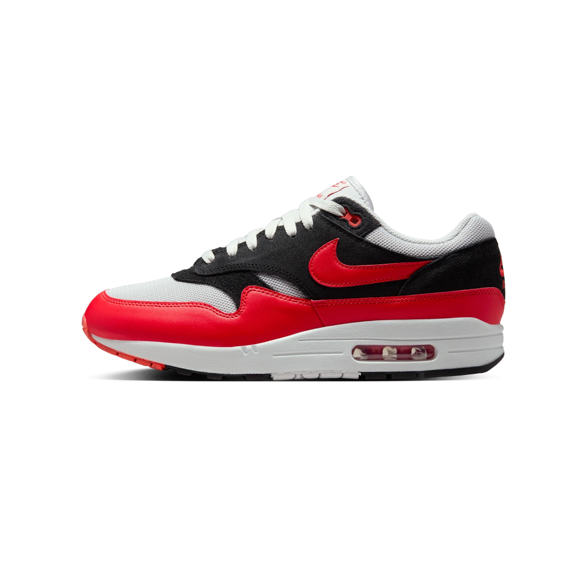 Side view of a Nike Air Max 1 sneaker with a red toe box and heel, black suede overlays, grey mesh panels, and a red swoosh logo, toe pointing left.