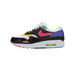 Side view of a Nike Air Max 1 sneaker with a black patent-look upper, pink swoosh, yellow accents, blue heel panel, teal trim, and visible Air cushioning in the sole.