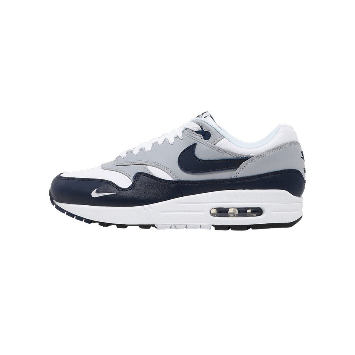 Side view of a navy, grey, and white Nike Air Max 1 sneaker with toe pointing left, showing the navy Swoosh logo and visible Air cushioning in the sole.