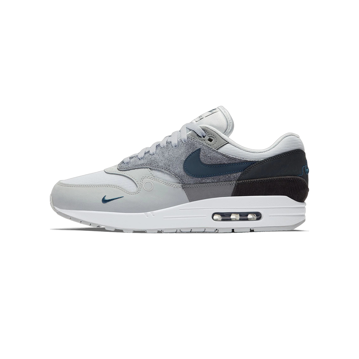 Side view of a grey and black Nike Air Max 1 sneaker with navy Swoosh logo, toe pointing left, showing white midsole and visible Air unit in the heel.
