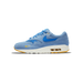 Side view of a single blue Nike Air Max 1 sneaker with the toe pointing left, showing a blue suede upper, a bright blue Swoosh, a small yellow Swoosh on the toe, and a white midsole with a visible Air unit.