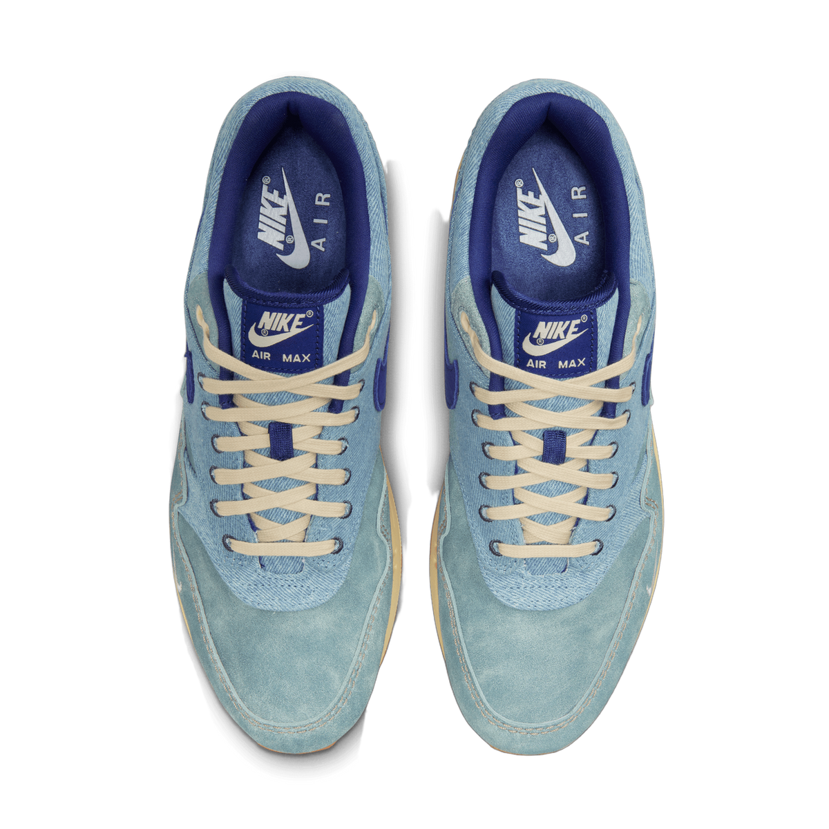 Top-down view of a pair of blue denim Nike Air Max 1 sneakers with cream laces, dark blue tongue tags, and gum soles.