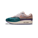 Side profile of a single Nike Air Max 1 sneaker with the toe pointing left, showing a teal-green toe box with a dotted pattern, a dusty pink and mauve upper with a rose-tan Swoosh, white laces, a purple midsole accent, and a cream-colored Air Max sol