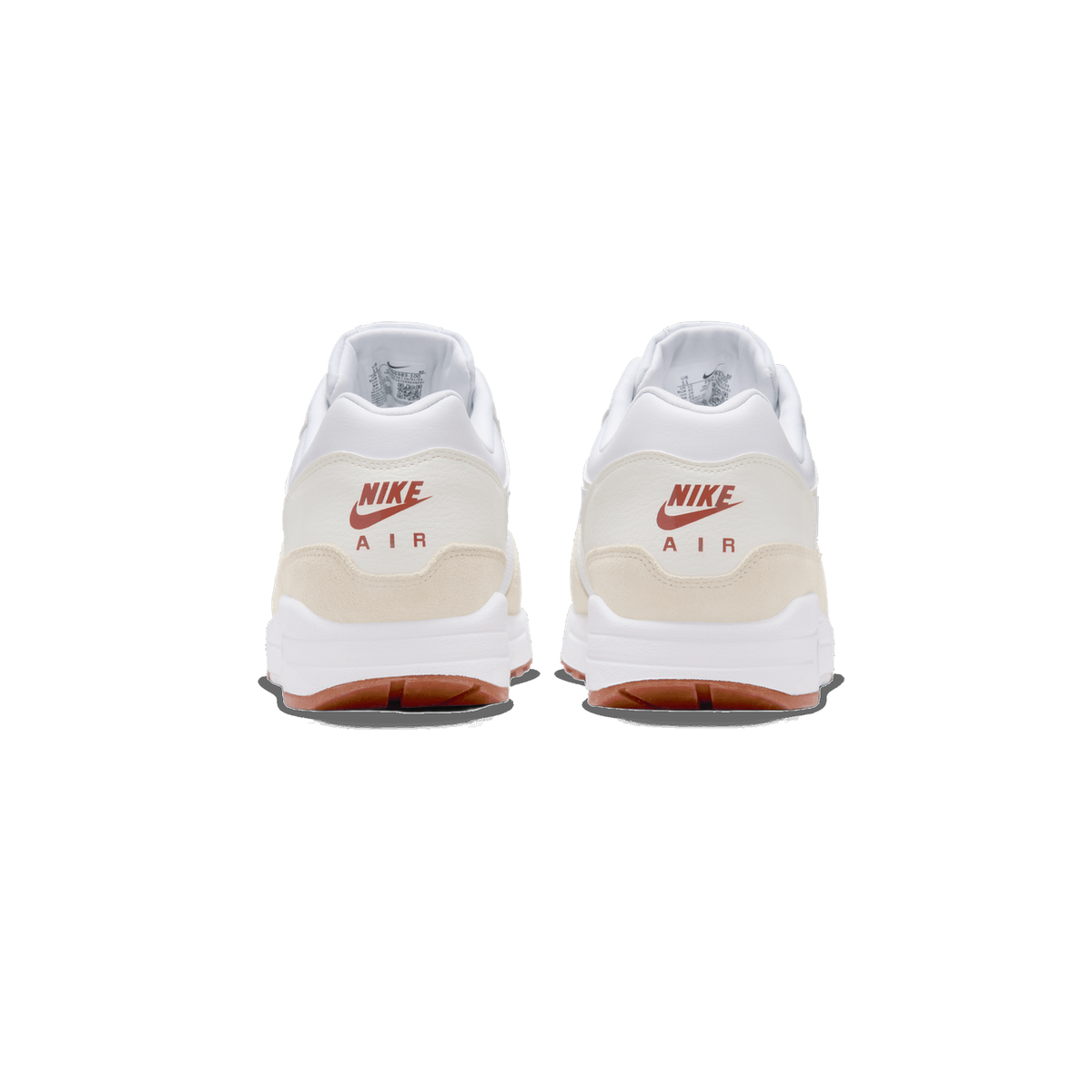 Rear view of a pair of white and cream Nike Air Max 1 sneakers standing side by side, showing the heel tabs with red Nike Swoosh and AIR branding and the red-brown outsole edges.