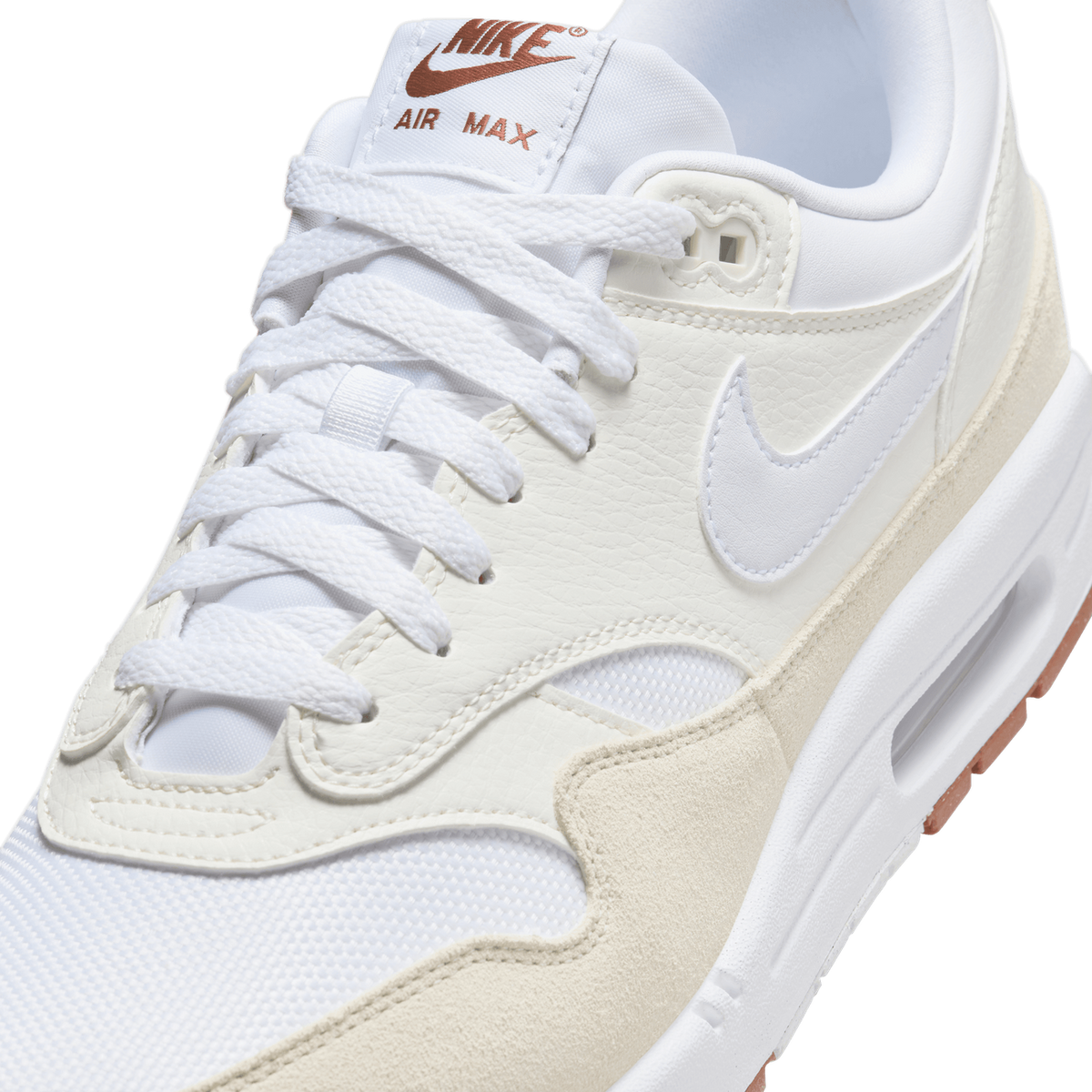 Close-up detail of a white and cream Nike Air Max sneaker showing the white laces, cream leather overlays with the Swoosh, the tongue label reading 'NIKE AIR MAX' in rust-brown lettering, and the cream suede panel along the midfoot.