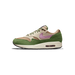 Side view of a Nike Air Max 1 sneaker with green suede overlays, tan mesh, cream accents, and a purple swoosh, with visible Air cushioning in the heel.