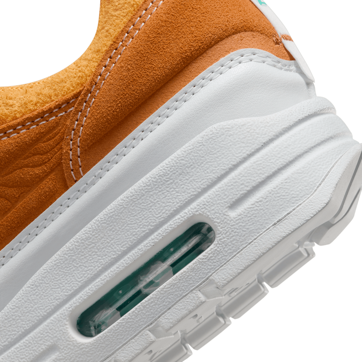 Close-up view of a sneaker's visible Air cushioning unit in the white midsole beneath an orange suede upper with stitched detailing.