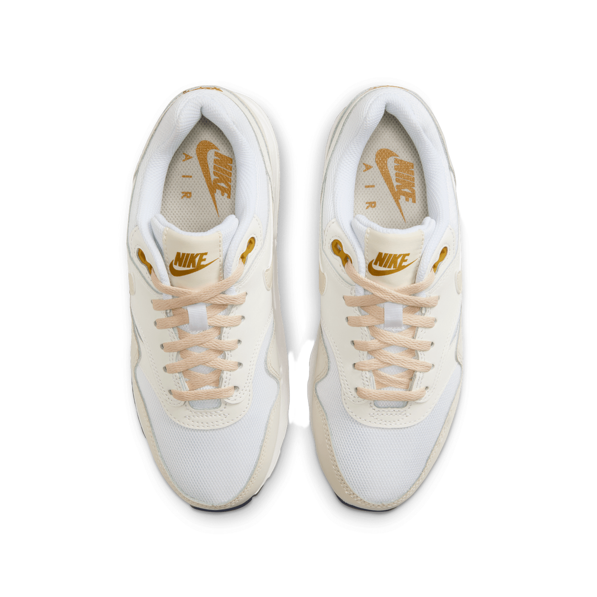 Top-down view of a pair of white Nike Air Max 1 sneakers placed side by side with toes pointing up, showing cream and tan overlays, tan laces, gold Nike logos on the tongues and insoles, and gold eyelet accents.