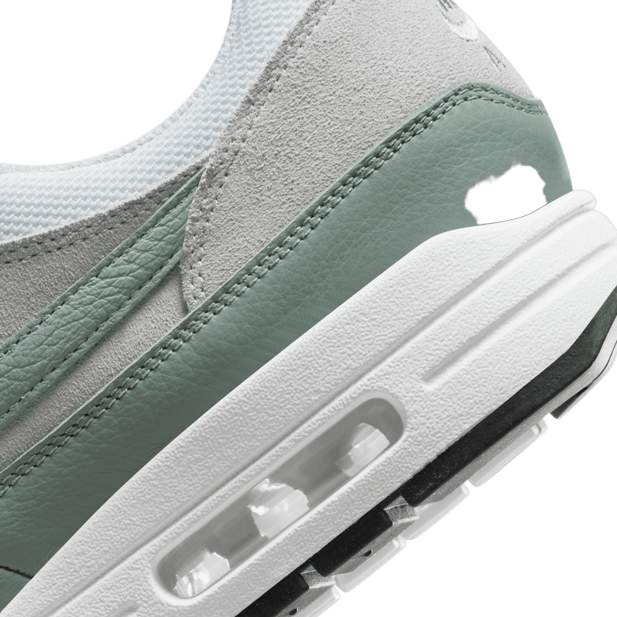 Close-up view of a white and green Nike Air Max 1 showing the visible Air cushioning unit in the midsole and suede overlay stitching.