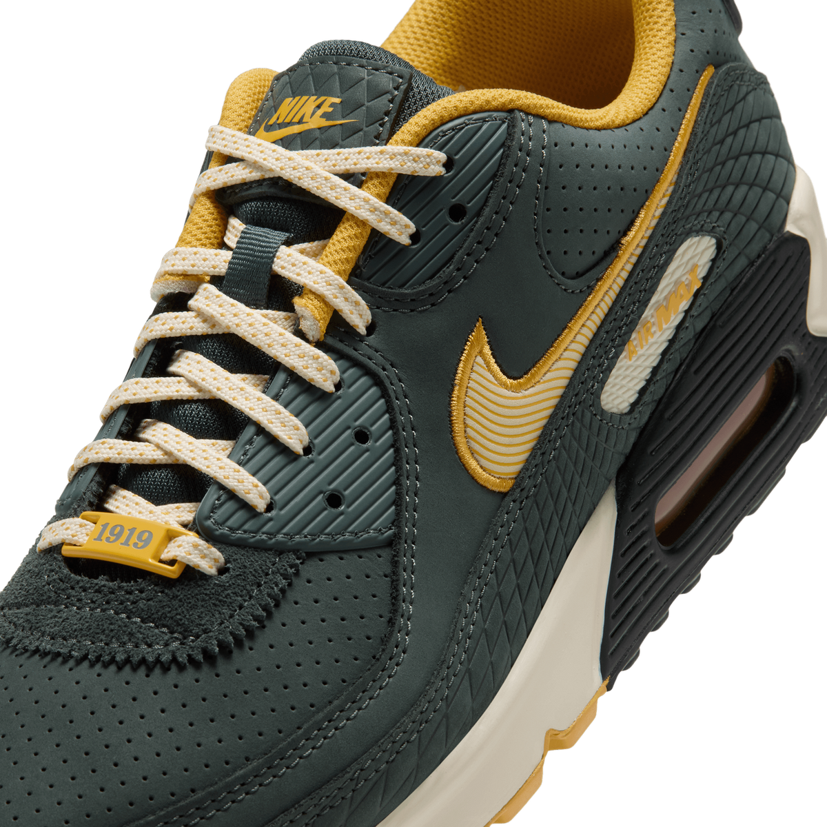 Close-up angled view of a dark green Nike Air Max 90 sneaker with gold accents, a striped swoosh, cream laces, and a yellow lace tag reading 1919