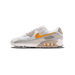 Lateral view of a white and grey Nike Air Max 90 sneaker with an orange Swoosh and visible Air unit in the heel, toe facing left.