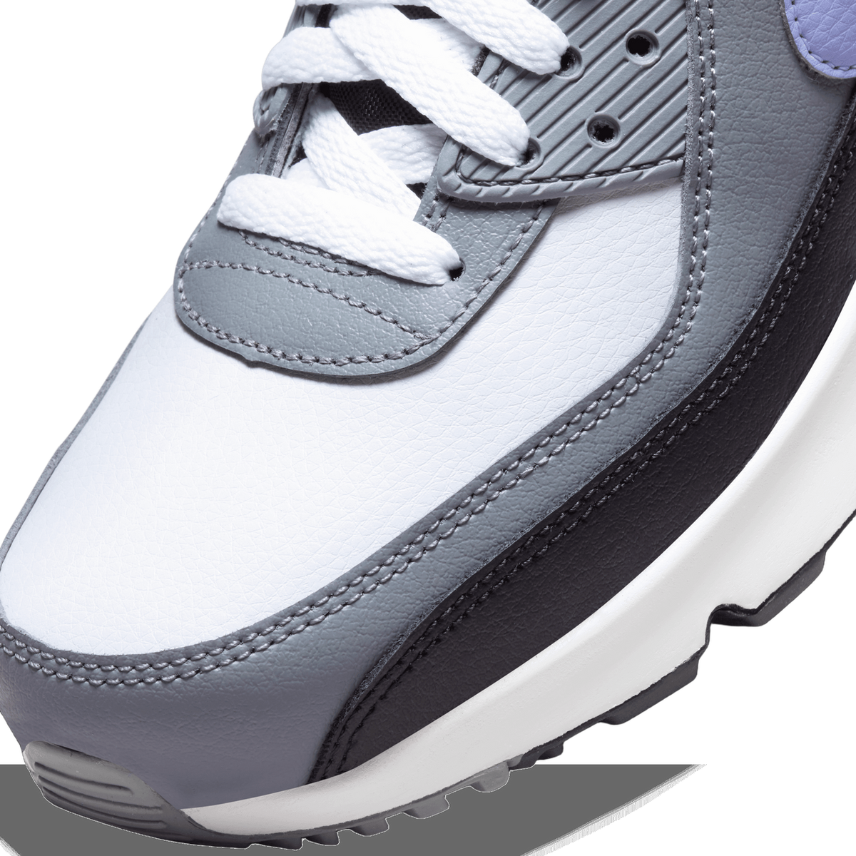 Close-up of the toe box and laces of a grey, white, and black leather Nike Air Max 90 sneaker with a purple heel tab visible in the background.