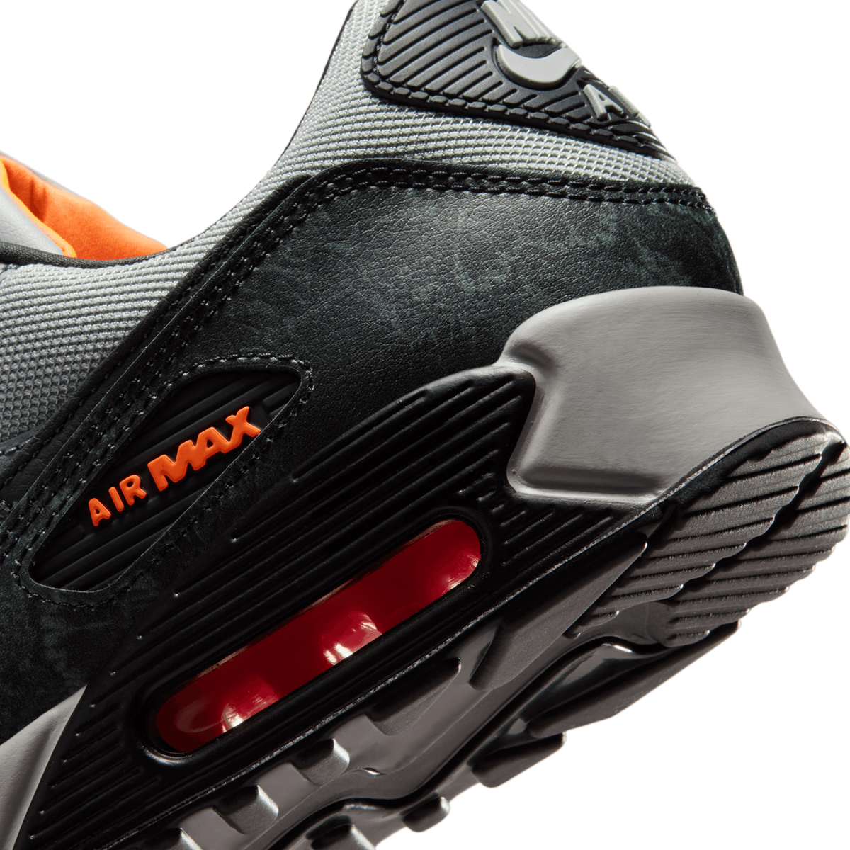 Close-up of a Nike Air Max 90 heel showing grey mesh upper, black leather overlay, visible red Air unit, and orange Air Max branding on the midsole.
