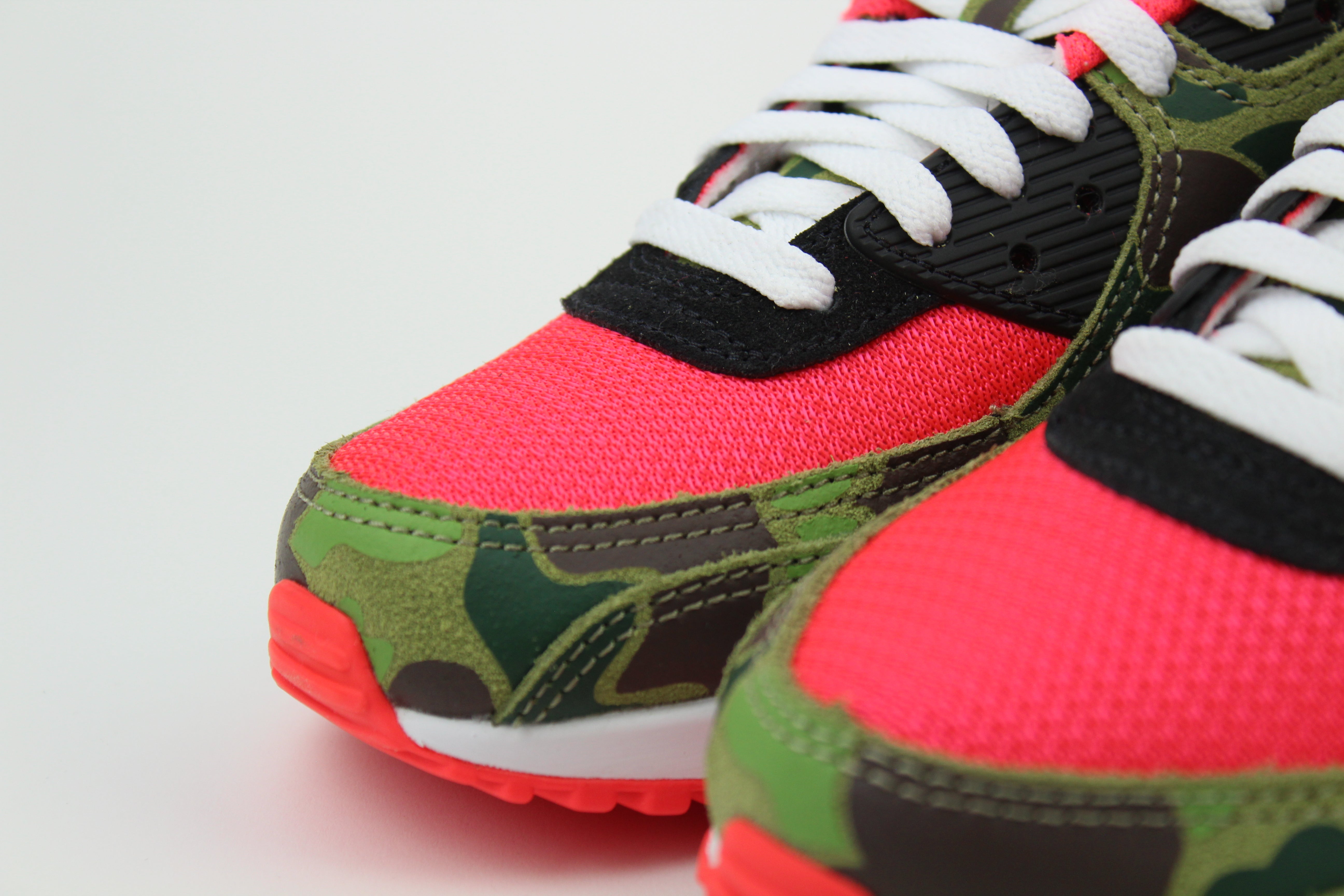 Close-up of Nike Air Max 90 'Reverse Duck Camo' sneaker, featuring bold reverse camo pattern, vibrant color accents, and signature Air cushioning, ideal for fashion-forward sneaker enthusiasts and collectors.