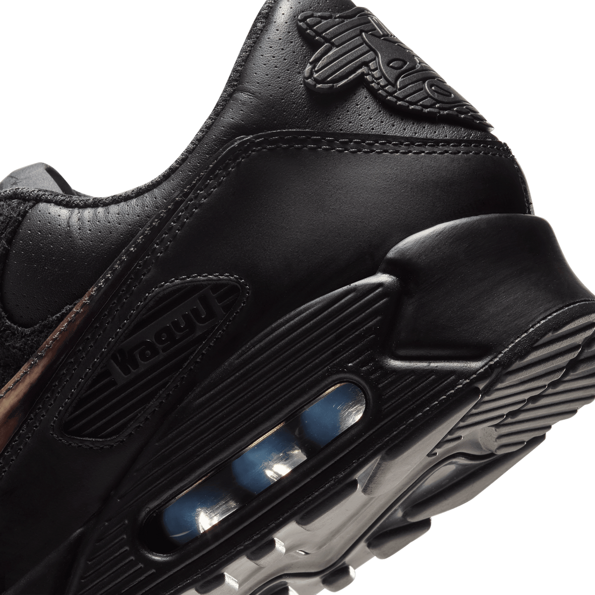 Close-up angled view of a black Nike Air Max 90 heel showing the visible Air unit with a blue bubble and a side text detail reading Wagyu.
