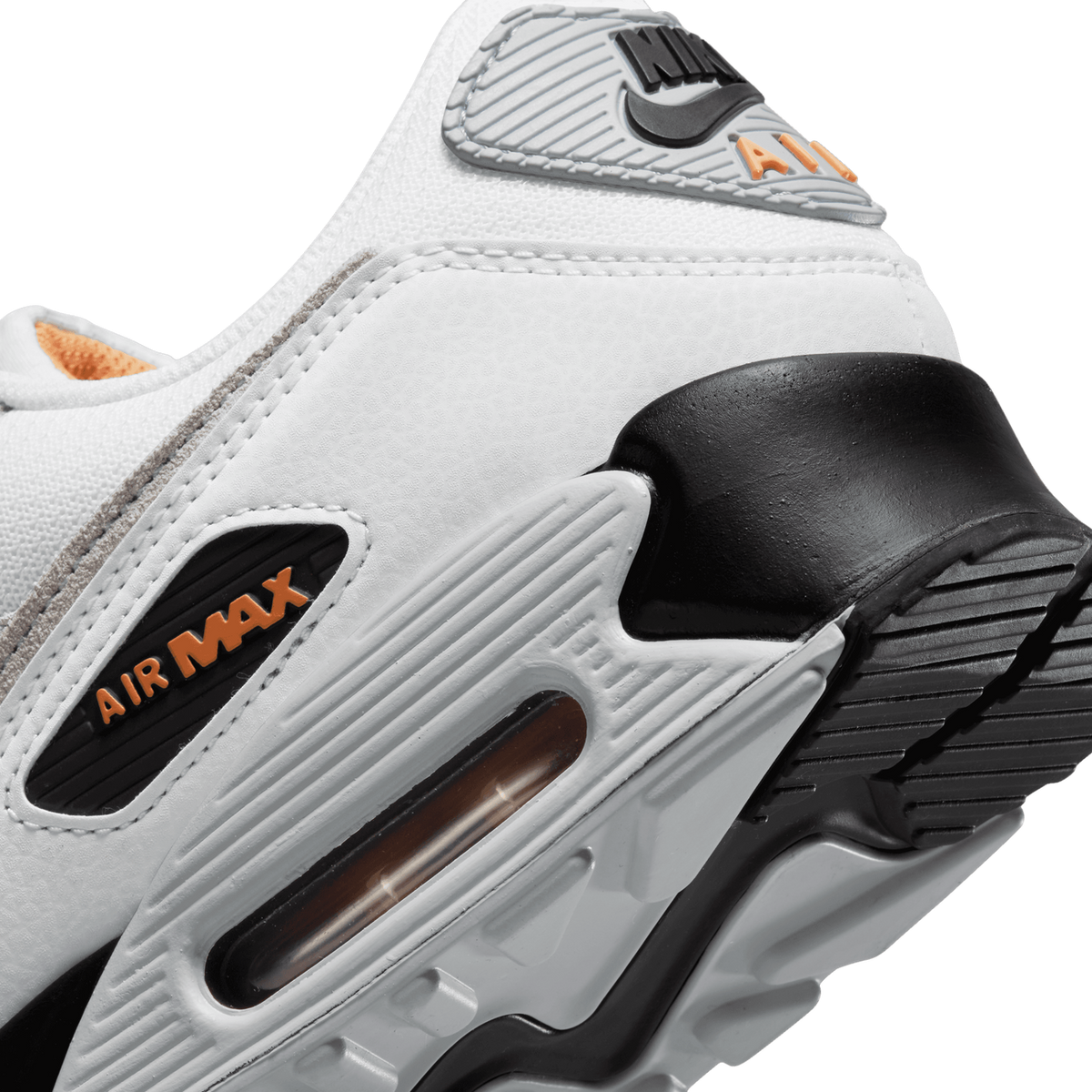Close-up of a white Nike Air Max 90 sneaker showing the heel Air unit, black and grey panels, and orange Air Max branding on the midsole.