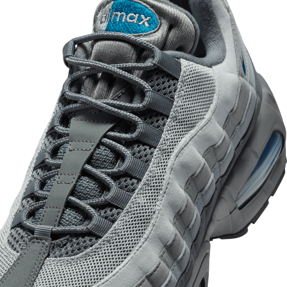 Close-up detail of a grey Nike Air Max 95 showing the laces, the teal-and-white 'max' embroidered tongue label, grey mesh panels, and a teal accent visible in the Air unit at the heel.