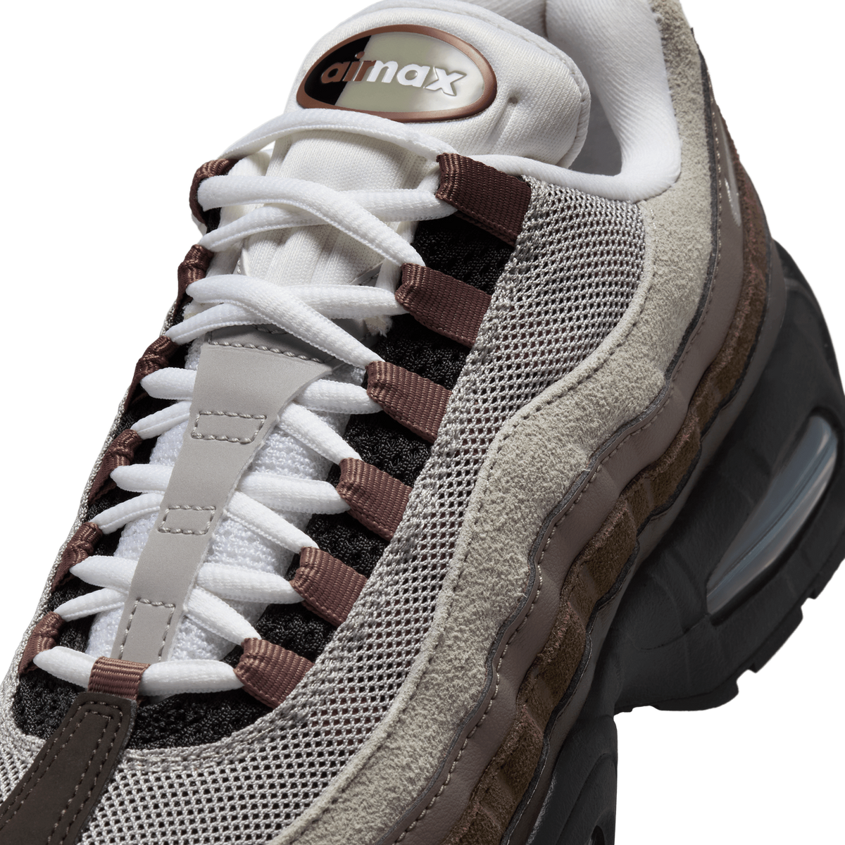 Close-up view of a Nike Air Max 95 sneaker in brown and grey tones showing the white laces, mesh panels, suede overlays, and Air Max tongue logo